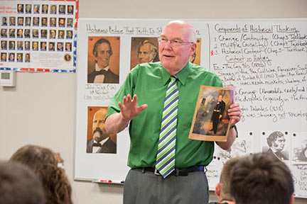 male teacher lectures while holding a book